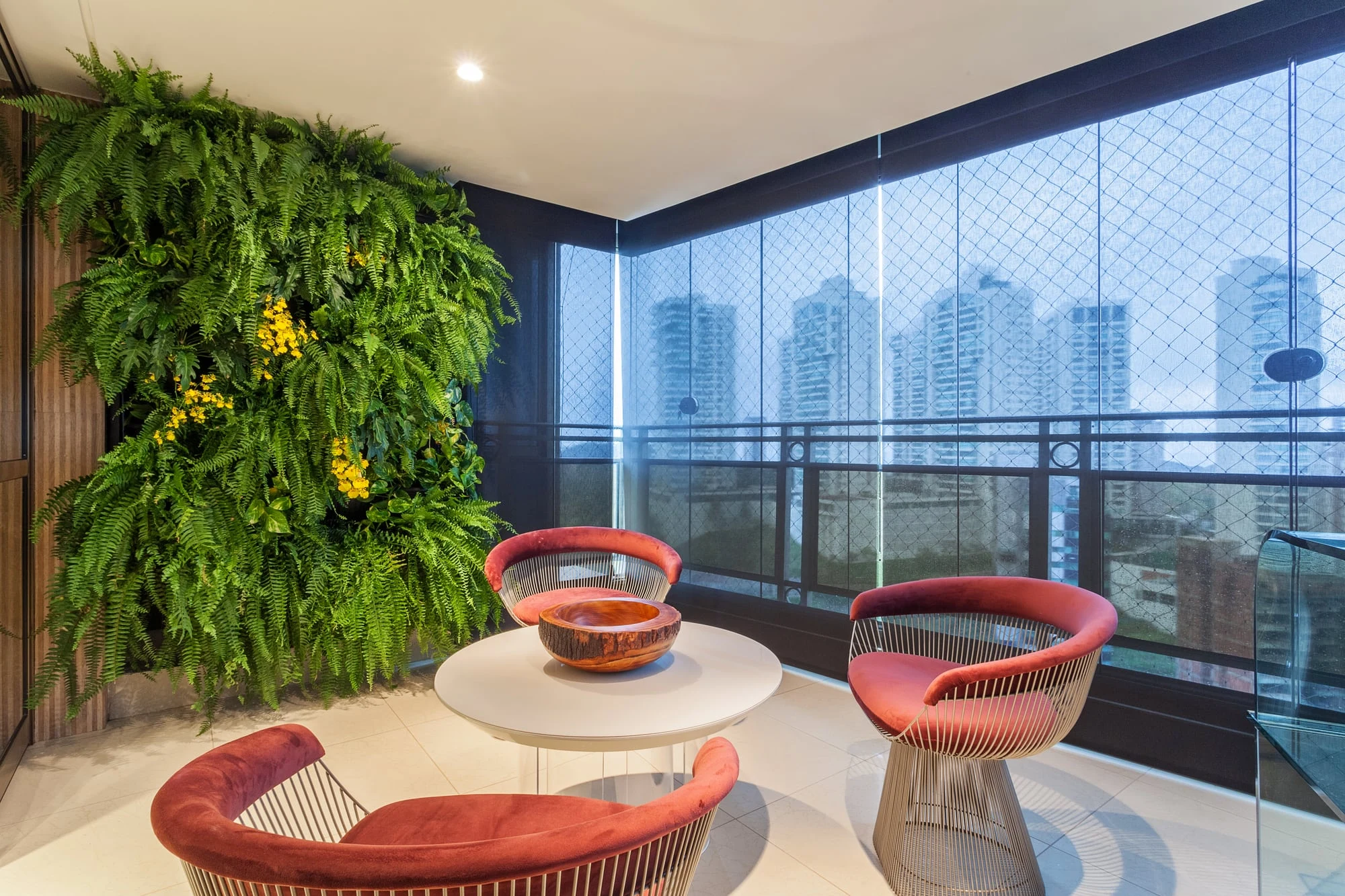 Varanda com jardim vertical, poltronas vermelhas e vista para a cidade